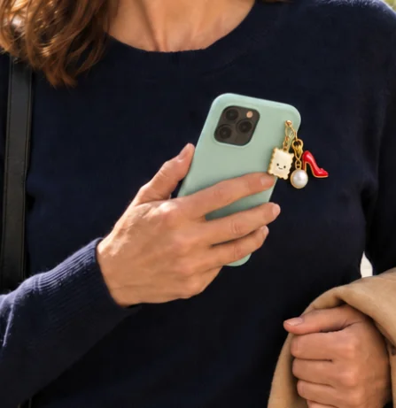 La raviole en charms doré accrochée à un smartphone vert, tenu en main