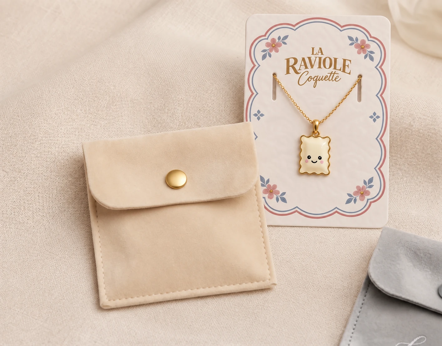 Le collier Raviole Coquette sur sa carte florale, accompagné de sa pochette beige sans initiales